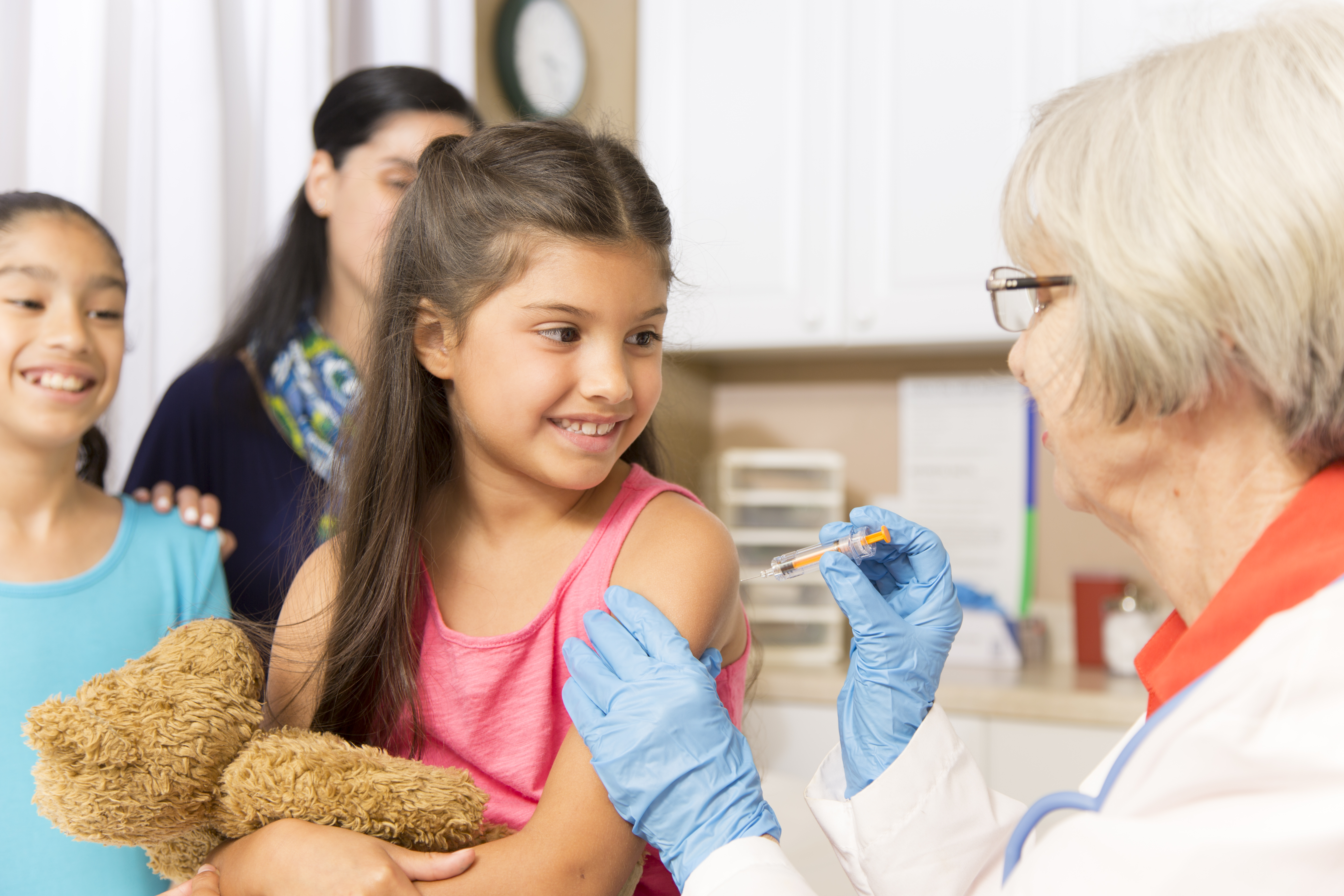 Girl getting vaccinated by doctor with sister and mother in background